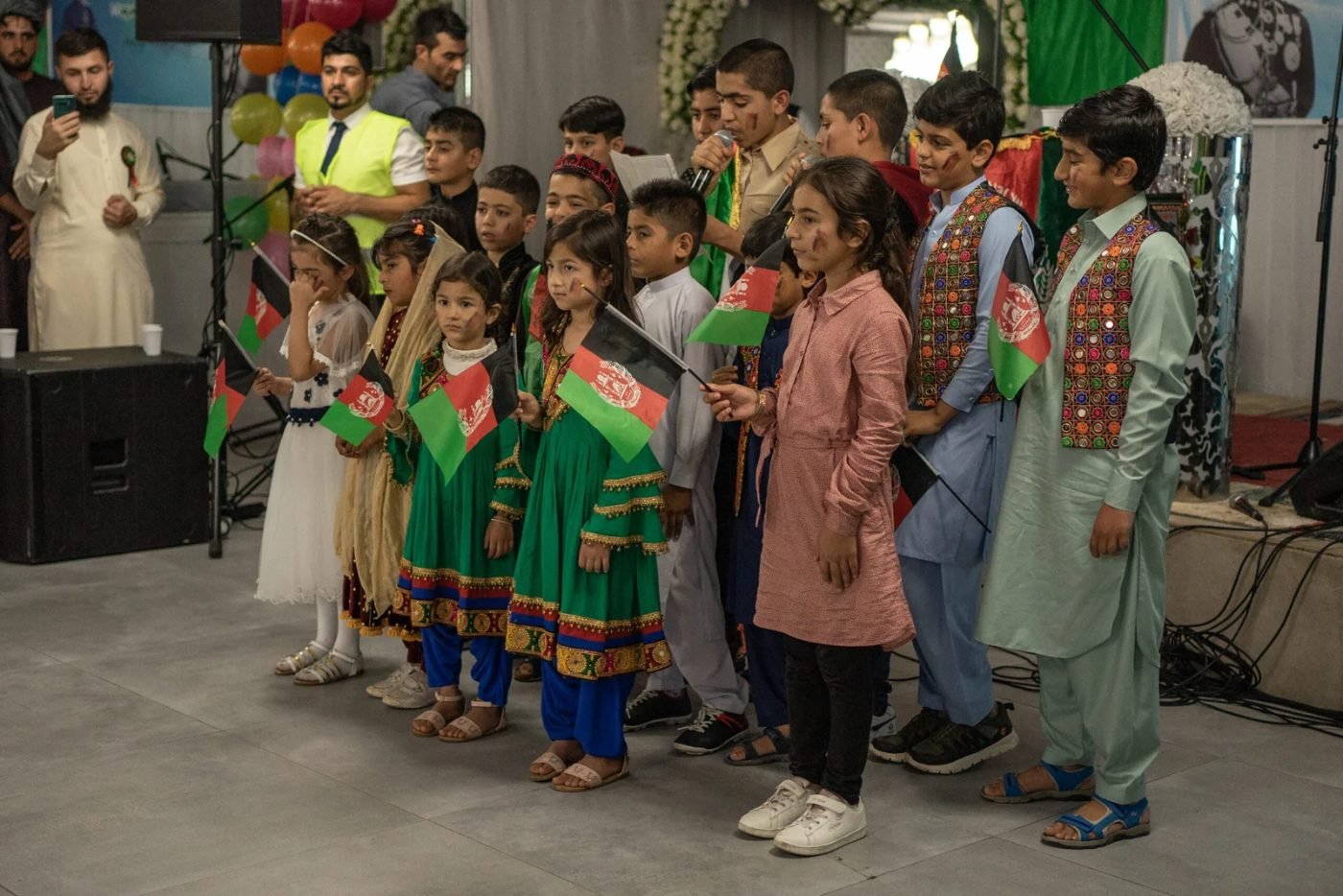 Des enfants de la diaspora afghane en tenue traditionnelle chantent avec des drapeaux afghans lors de la Fête de l